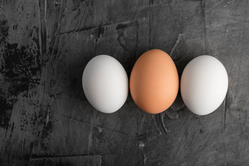 Three eggs, two white and one brown on a black background. Copy space