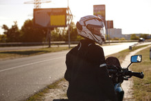 Waist-deep Shot Of A Biker In A White Helmet Near The Road. Resting On The Motorbike. Blurred Road.