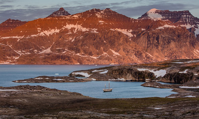 Wall Mural - Arctic landscape in summer with high mountains, wet meadow and a sailing ship in Scoresby Sound, East Greenland