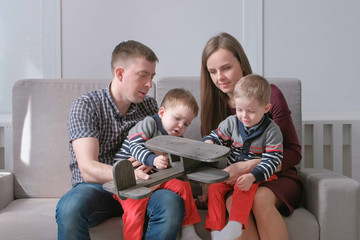 Family mom, dad and two twin brothers read books sitting on the sofa. Family reading time.