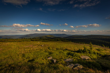 Wall Mural - View from peak of Velky Keprnik to Jeseniky in background and green grass in foreground with blue cloudy sky.