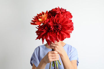 Woman holding bouquet of beautiful dahlia flowers against light background