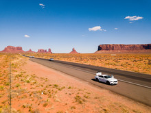July 30, 2018. Monument Valley National Park, Utah, USA. White Ford Mustang Parked By The Side Of The Road At Monument Valley National Park With An Amazing View On The Infinite Road Through The Desert