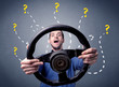 © ra2 studio - Young man holding black steering wheel with question marks around him