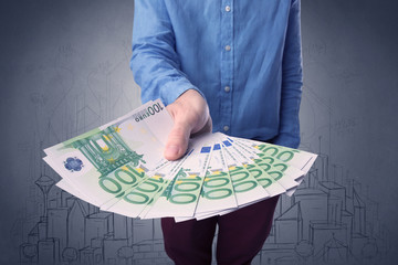 Wall Mural - Young businessman holding large amount of bills with grungy drawings of a city and numbers behind him