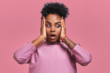 Wall Mural - Gorgeous beautiful female with dark skin, opens mouth wide and expresses surprisement, receives shocking news, isolated on yellow studio background with pink wall