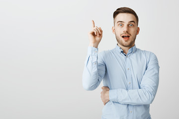 Wall Mural - Guy got excellent idea sharing with team. Enthusiastic excited good-looking male in formal blue shirt raising index finger in eureka gesture holding breath and opening mouth while adding suggestion