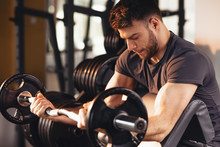 Handsome Man Doing Biceps Lifting Barbell On Bench In A Gym
