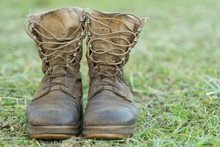 Close Up Front View Of A Pair Of Muddy Boots Isolated On Green Grass Ground.