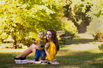 Happy young mother playing with baby in autumn park with yellow maple leaves. Family walking outdoors in autumn. Little boy with her mother playing in the park in autumn.