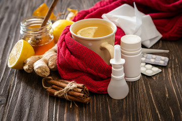 Medical care concept - ginger honey and lemon tea with drugs, pills and spray on wood background