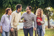 © Mediteraneo - Four happy smiling young friends walking outdoors in the park holding digital tablet