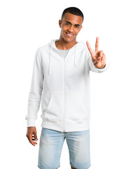 Dark-skinned young man with white sweatshirt smiling and showing victory sign on isolated white background