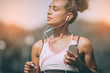© Andrii - Serious female jogger looking confident. Young fitness woman listening music with headphones after training outdoors at stadium track. Girl runner listen music in earphones from smartphone