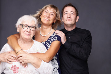 Wall Mural - Multi generation concept. Family portrait of mature wrinkled woman dressed in stylish shirt, surrounded with love of  daughter and son who came to congratulate pretty elderly lady with anniversary.