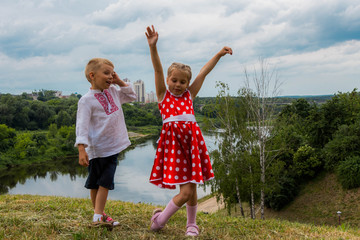 two carefree children, a boy and a girl dancing on a hill above the river