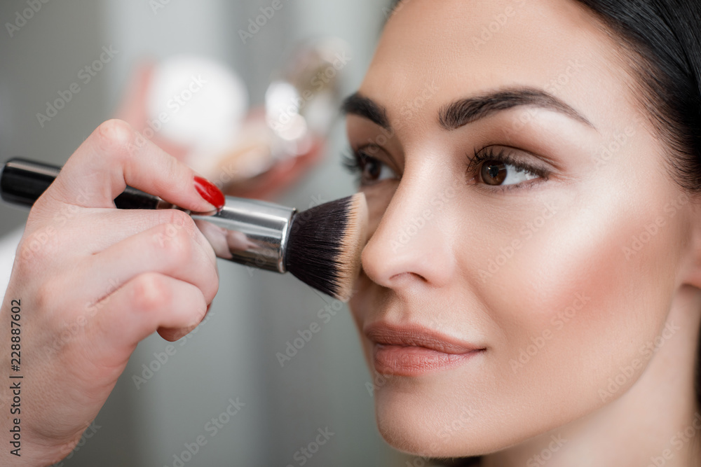 Close up of makeup artist applying light layer of matting powder while using professional brush for lady - obrazy, fototapety, plakaty 