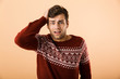 Image of uptight man 20s with stubble wearing knitted sweater grabbing head, isolated over beige background
