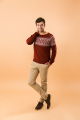 Canvas Print - Full length image of brunette man 20s with bristle wearing knitted sweater smiling, isolated over beige background