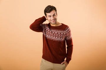 Canvas Print - Image of cheerful man 20s with bristle wearing knitted sweater smiling on camera, isolated over beige background