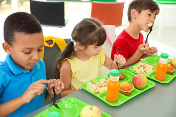 Children sitting at table and eating healthy food during break at school