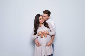 Poster - Pregnant woman and her husband holding little shoes on color background