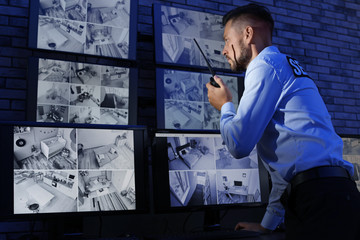 Wall Mural - Male security guard with portable transmitter monitoring modern CCTV cameras indoors