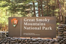 Daytime Photo Of A Great Smoky Mountains National Park Entrance Sign With Stone Surrounding And Trees And Sunshine In The Background
