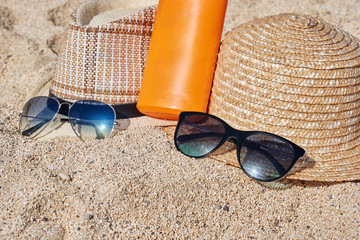 Two sunhats, sunglasses and sunprotection cream are laying on the sand.