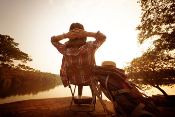 Wall Mural - Backpack woman sitting beside the river with sunset background