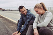 Smiling young couple sitting on a curb after jogging together