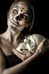 Wall Mural - Portrait of the woman with halloween makeup close up. Playiong with skull. Isolated image on black background with beautiful studio light.