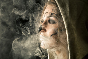 Wall Mural - Stylish woman with halloween make up posing isolated on black background with the smoke around her and beautiful studio light.
