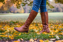 Woman Wearing Brown Leather Boot And Walking In Fallen Leaves. Fashion Model In Autumn Park 