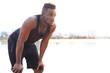 © ty - Tired African man in sports clothing looking away while standing outdoors, in beach at sunset or sunrise.