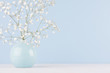 Spring branch with small white flowers in blue sphere vase in soft light blue modern interior, on a white table.