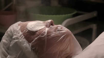 Wall Mural - The girl's face under the transparent film on the procedure of pores expansion and skin steaming. Hot steam is directed to the head of a woman. Camera movement from top to bottom.