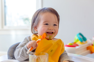 Wall Mural - Happy toddler boy smiling while eating a meal