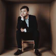 Young Businessman In Black Suit In Cardboard Box.