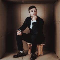 Young Businessman in Black Suit in Cardboard Box.