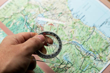 Hand holding a compass with a map in the background. Orienteering concept image. 