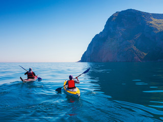 Kayaks. Couple kanoeing in the sea near the island with mountains. People kayaking in the ocean.