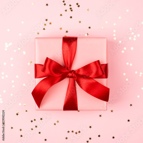 Pink gift box with red bow on pink background with sparkles. Holiday concept.