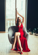 © kharchenkoirina - hot young proud woman, dressed in a long scarlet red long dress and red high-heeled shoes. Gently raises her hands up in a room with window to the floor in loft style. image for girls at graduation