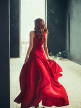 Slim Girl With Red Hair Runs Into A Fashionable Room In A Loft Style With Dark Black Walls And Window To The Floor, Dressed In A Long Flying Dress In Scarlet Red Color, Art Processing Photo With No