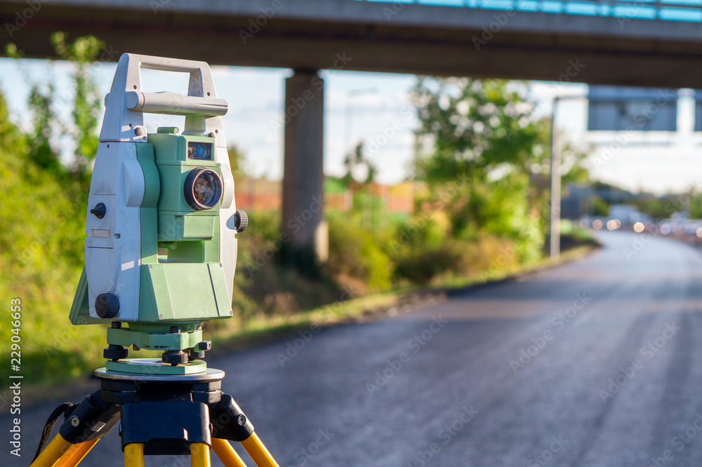 Surveyor equipment (theodolit or total positioning station) on the construction site of the motorway or road with bridge in background - obrazy, fototapety, plakaty 
