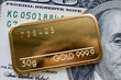 © vladk213 - Minted gold bar weighing 50 grams against the background of a dollar bill.