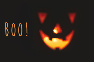 Boo! text, spooky sign. Happy Halloween. Blurred Pumpkin with scary glowing face on black background isolated. Jack o lantern glowing pumpkin in dark. Season's greeting card