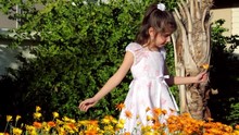 Little Girl Cautiously Spins In Flowers Then Stops To Smile For Camera.