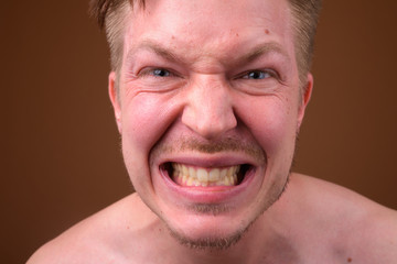 Young handsome man shirtless while grooming against brown backgr